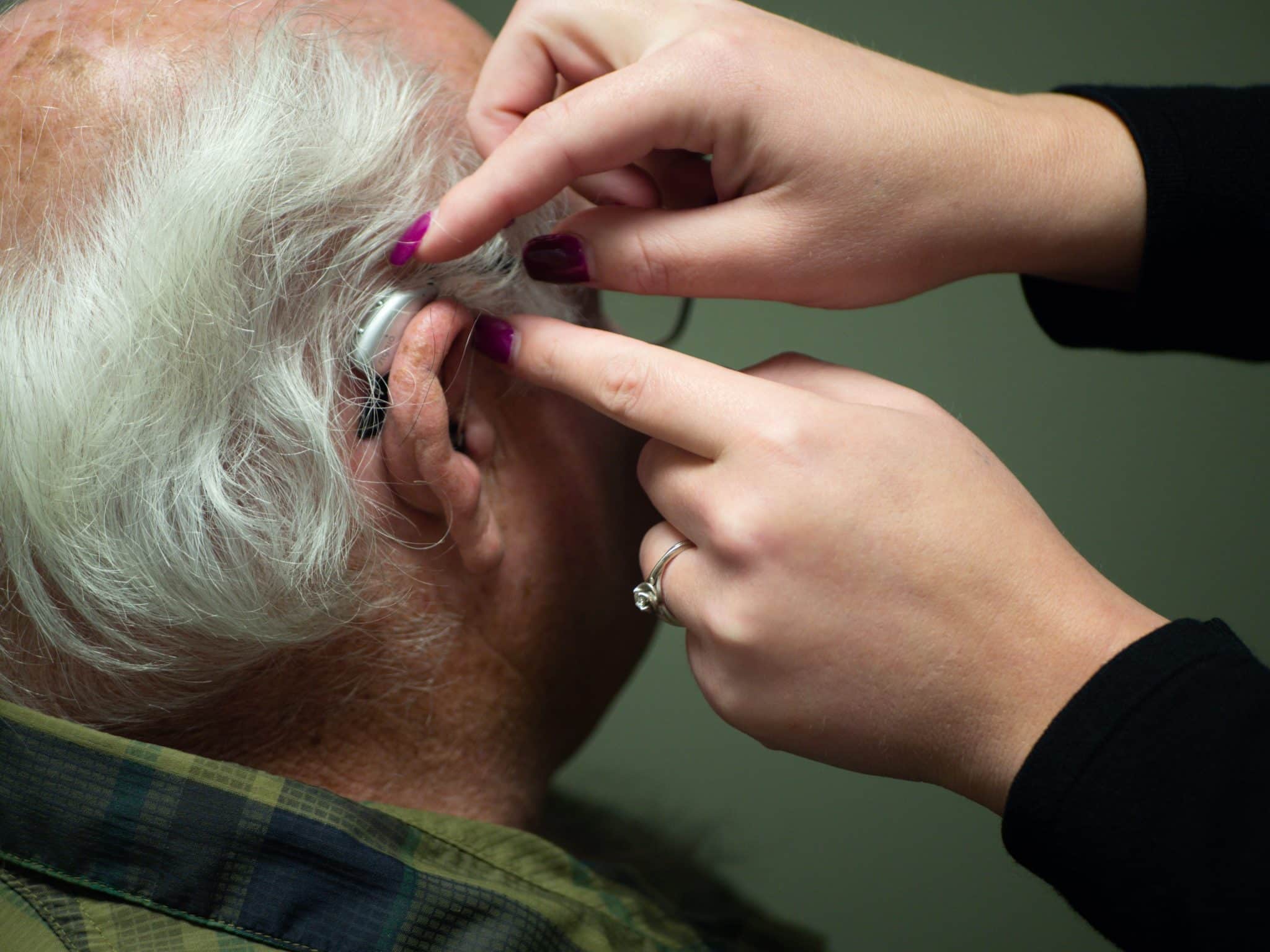 Women puts hearing aid on older gentleman