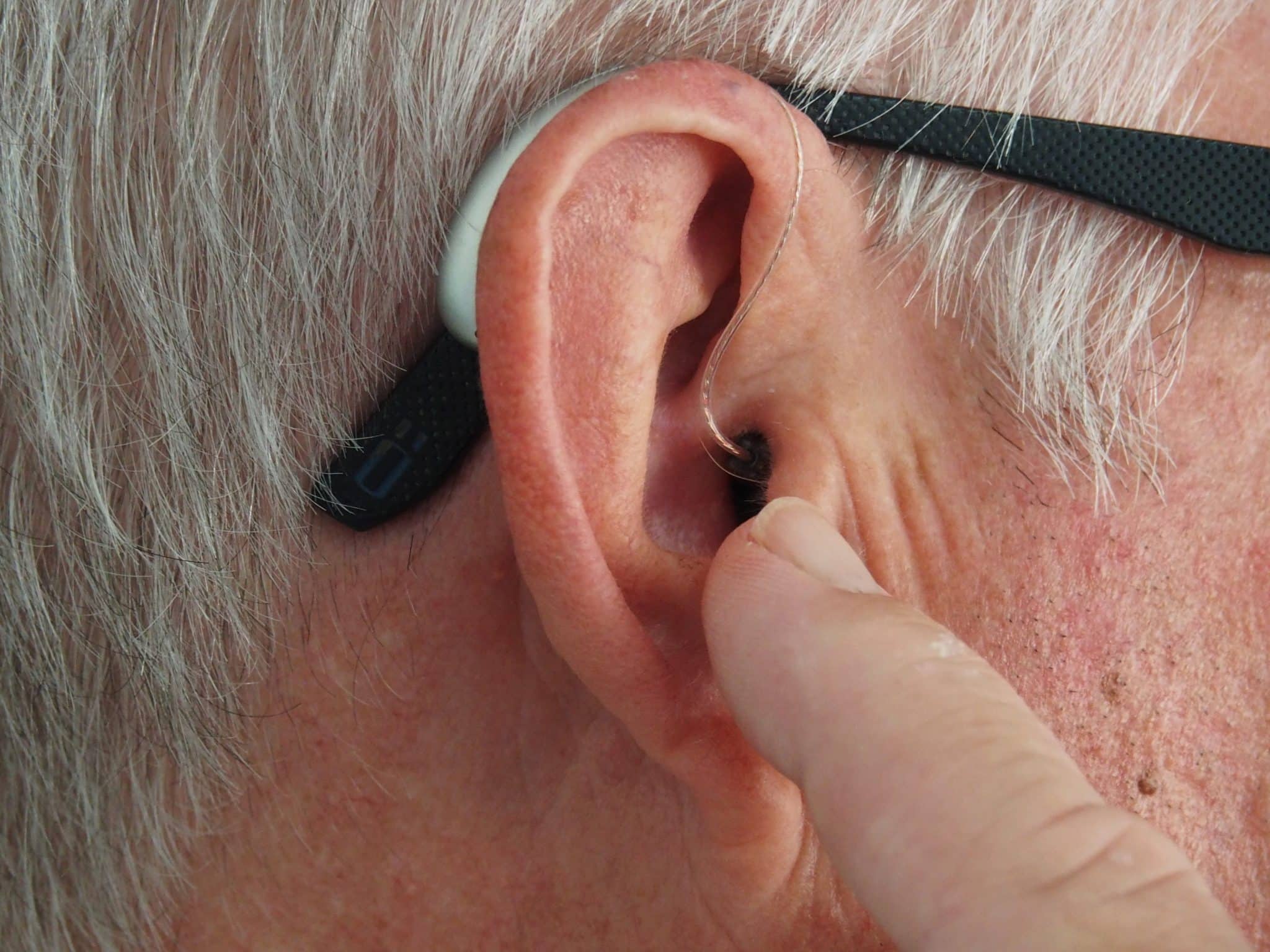 A older-aged man with cookie bite hearing loss adjusts his hearing aids